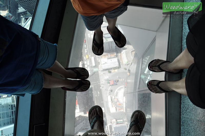 Our feet on the glass floor of Sky Tower with a view of the street below - Auckland New Zealand - Woodward Culture Travel Guide