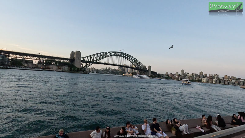 Sydney Harbour Bridge at dusk with people relaxing on the seats in the foreground - Australia - Woodward Culture